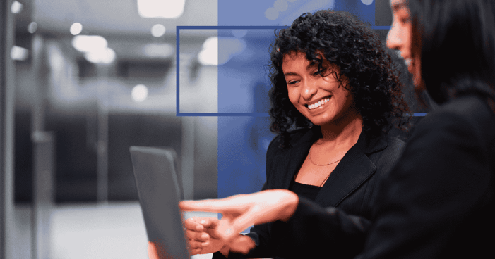 Two professionals look at a laptop together with blue design elements in the background.